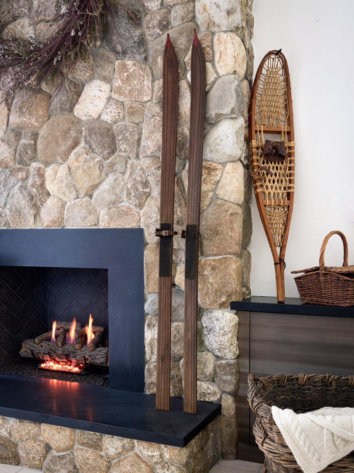 Wooden skis and snowshoes against a stone fireplace with a basket on a shelf.