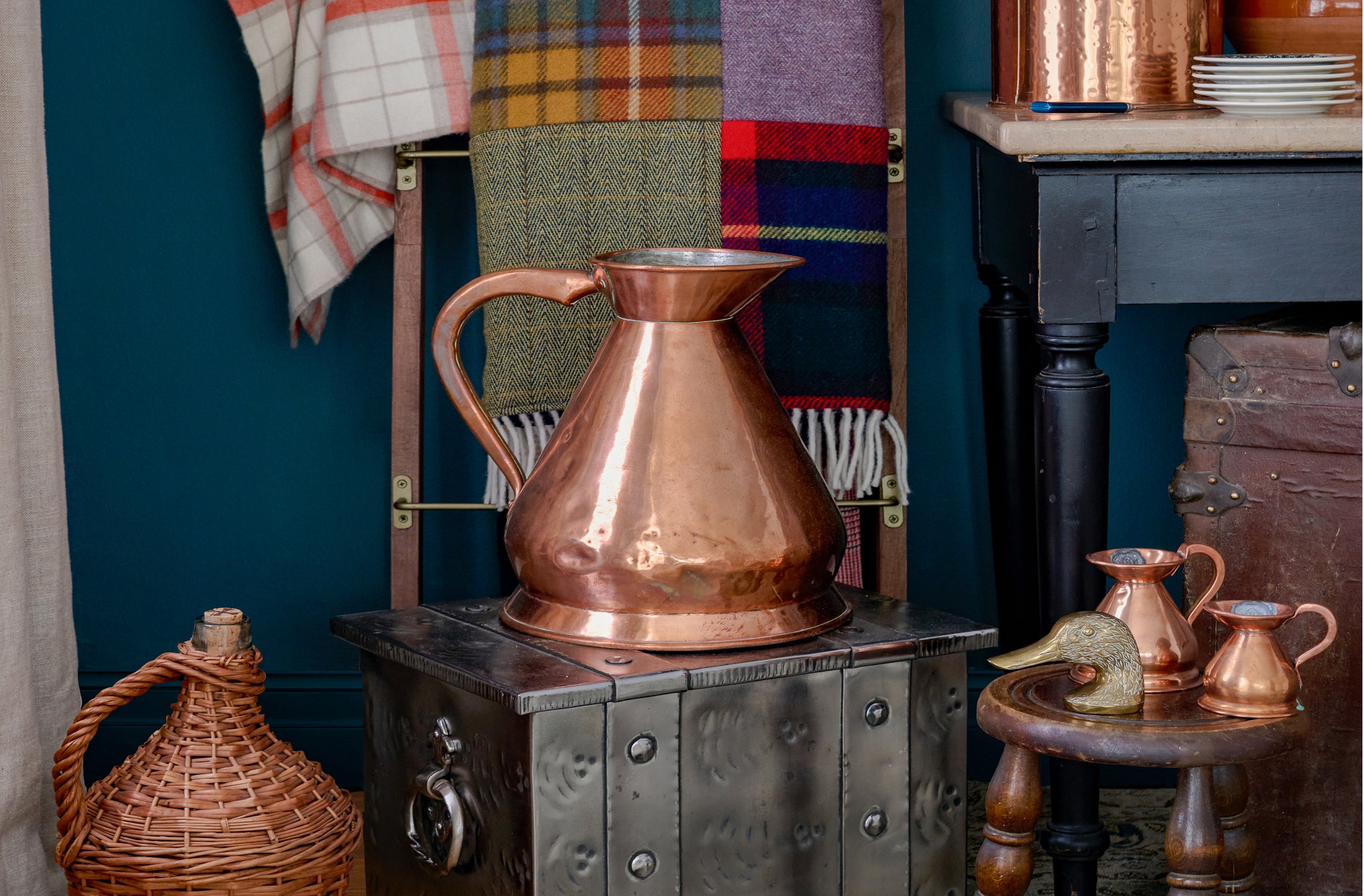 Copper pitcher on a metal stove with plaid fabrics in the background