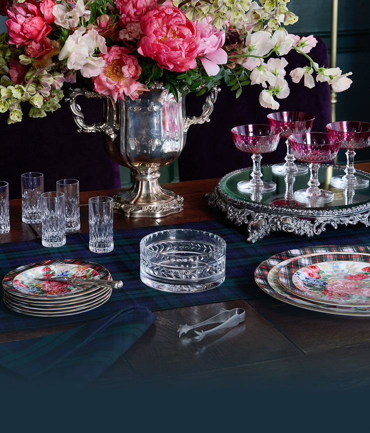 Decorative table setting with floral arrangement, crystal glasses, and plates on a dark surface.