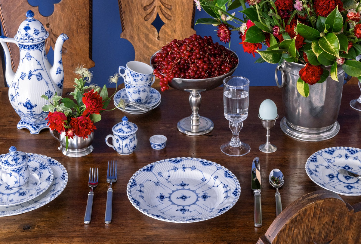 Dining table set with blue and white dinnerware, flatware, and floral arrangements.