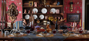  Dining room with a table set for a fondue meal, red wallpaper, vintage copper cookware, and ski-themed decor. 
