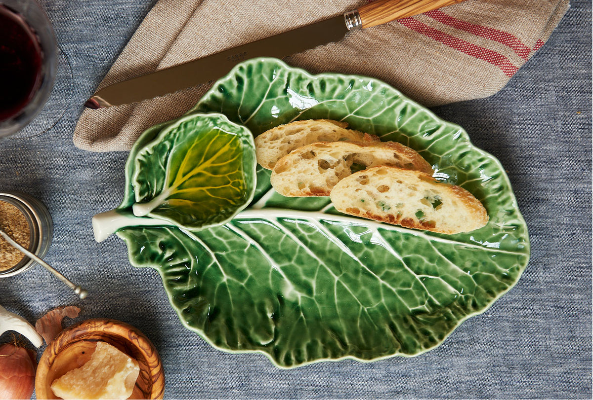 Green cabbage leaf-shaped ceramic plate with bread on a table setting.