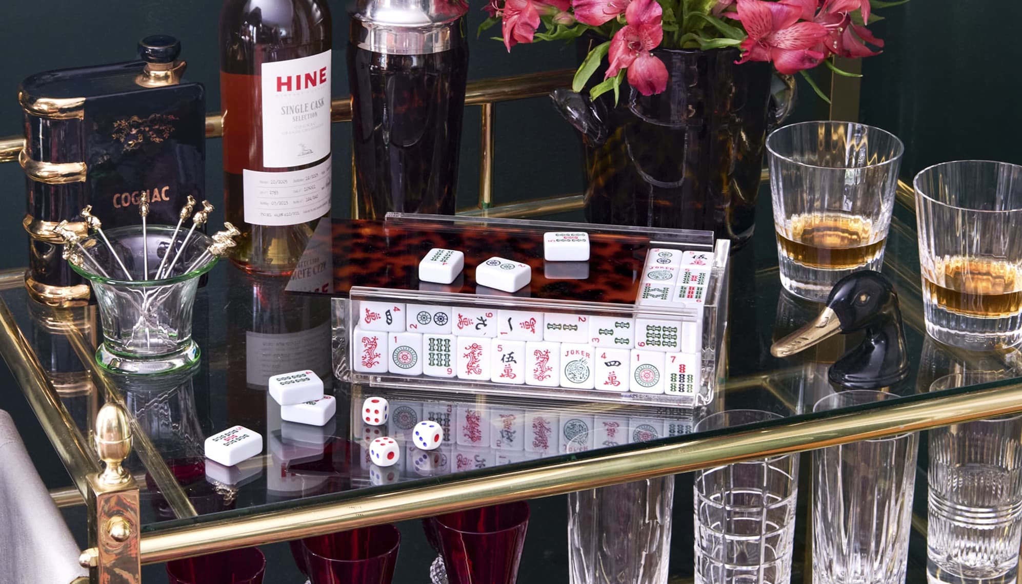 Glass bar cart with mahjong set and bar accoutrements.