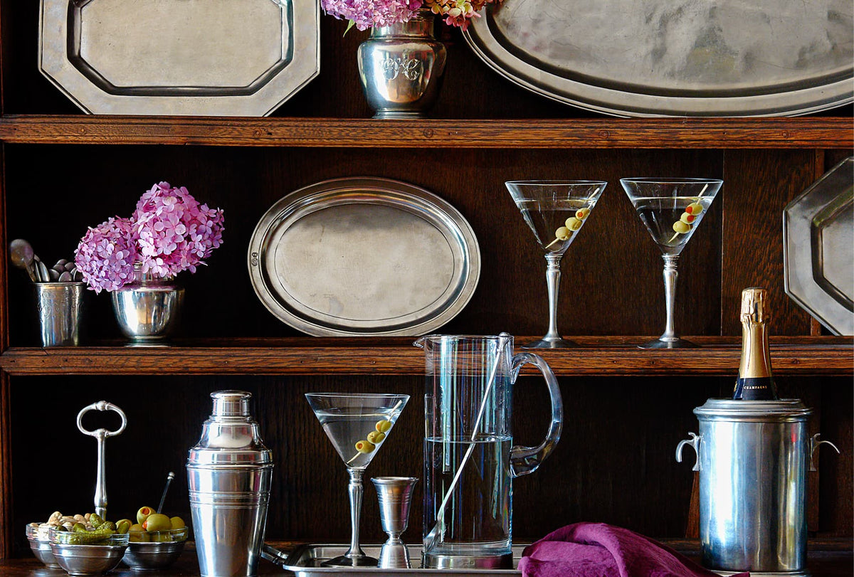 Bar setup with cocktail glasses, shaker, and platters on a wooden shelf.