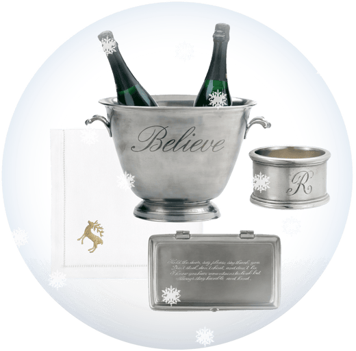 A collage of personalized gifts on a white background with a circular light-blue shadow. The set includes a champagne bucket engraved with the word 'Believe' with two champagne bottles, an embroidered napkin with a gold reindeer, an engraved napkin ring, a rectangular pewter box, on a white background. Weston Table.