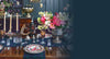 Decorative table setting with flowers, plates, and cutlery against a dark blue wall.